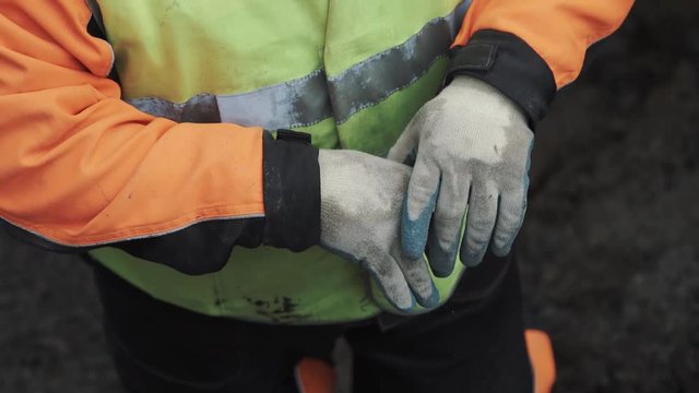 Worker in green vest correcting work gloves on hands in the ditch