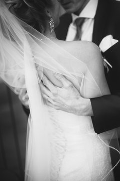 groom young man hugging the bride in a white dress and a long veil, earrings in behind his back, hands close-up, rear view, black and white photo