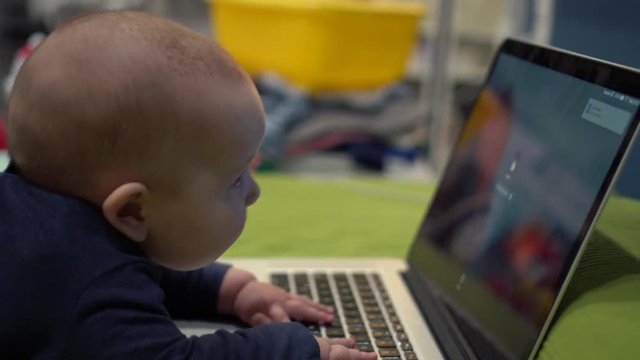 Baby crawls towards the sreen of a big laptop. Handheld shot
