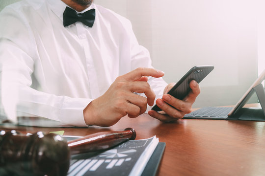 Justice and Law context.Male lawyer hand working with smart phone,digital tablet computer docking keyboard with gavel and document on wood table