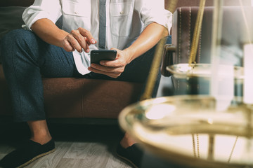 Justice and Law context.Male lawyer hand sitting on sofa and working with smart phone,digital tablet computer docking keyboard with gavel and document on living table at home,filter effect