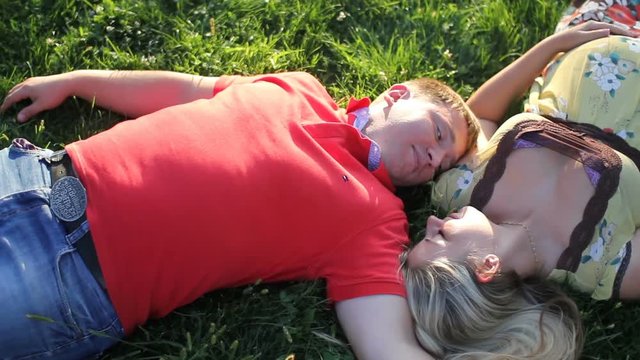 loving couple laying on grass in park. man kissing pregnant woman