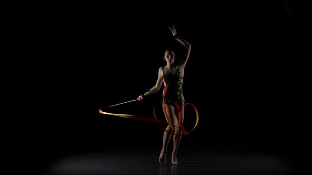 Gymnast gracefully move with a ribbon in his hands. Black background