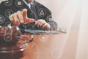 justice and law concept.Male judge in a courtroom with the gavel,working with smart phone,digital tablet computer docking keyboard,brass scale,on wood table,virtual interface graphic icons diagram
