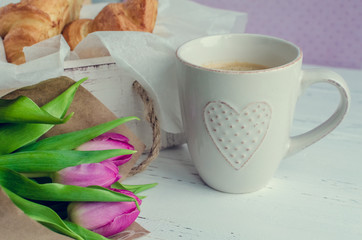 Cup of coffee with bouquet of pink tulips and croissants