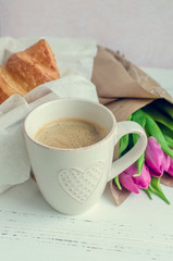 Cup of coffee with bouquet of pink tulips and croissants