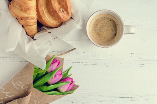 Cup of coffee with bouquet of pink tulips and croissant