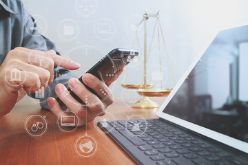 justice and law concept.Male lawyer in office with the balance brass scale,hand working with smart phone and digital tablet computer on wooden desk,virtual graphic icons screen diagram