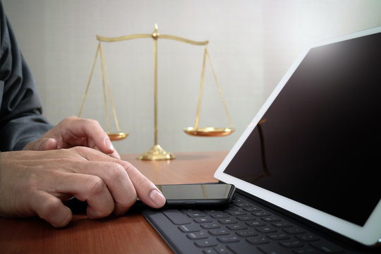 justice and law concept.Male lawyer in office with the gavel,working with smart phone and digital tablet computer and brass scale on wood table