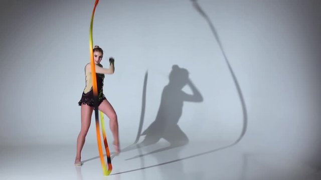 Rhythmic gymnast doing acrobatic moves with the tape. White background. Slow motion