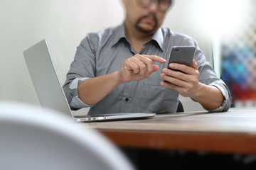 Businessman using smart phone for mobile payments online shopping with laptop computer on wooden desk in modern office