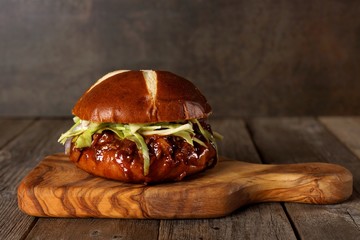 Pulled pork burger on pretzel bun on a serving board with wood background