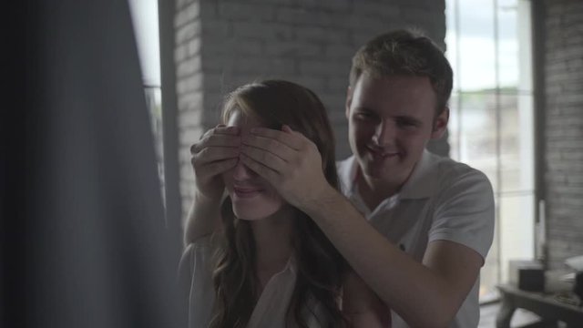 man closes his is girlfriend's eyes to make surprise.