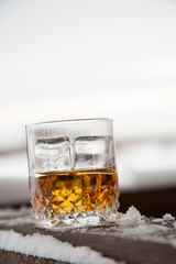 glass of whiskey with ice in snow on winter background.