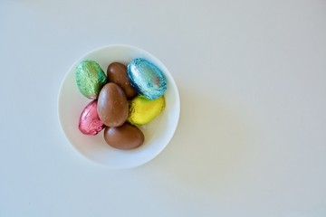 Colourful chocolate Easter eggs on the white plate on the white table