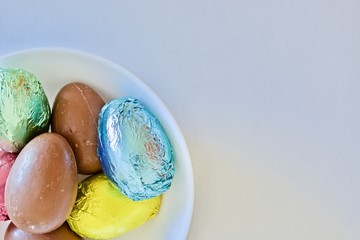 Colourful chocolate Easter eggs on the white plate on the white table