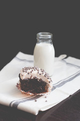 Chocolate chip cupcakes with vanilla cream cheese frosting on a tea towl with a glass bottle of milk