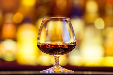 Cognac in a glass on a background of bright lights. Traditional French drink.