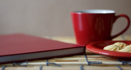 Hot coffee, cookies and a book on a wooden table.