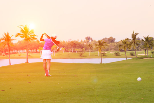 female golf player swinging golf on fairway during sunset with flare