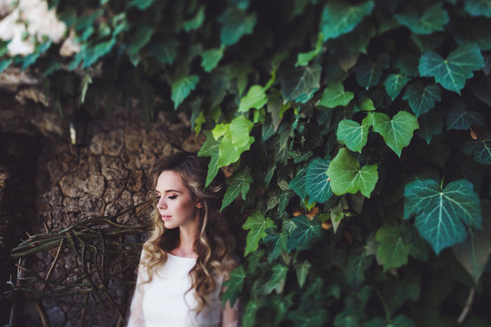 Pretty portrait of woman with long blonde curly hair in green ivy