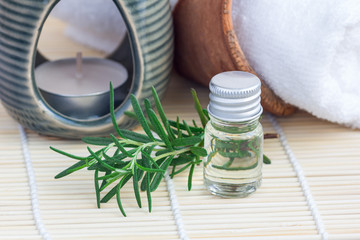 Rosemary essential oil in glass on woven mat with spa background, horizontal