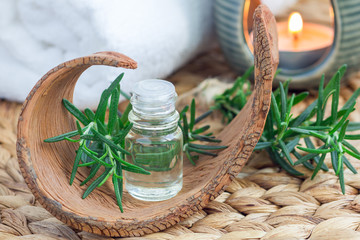 Rosemary essential oil in glass on woven mat with spa background, horizontal