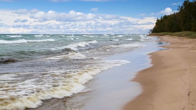 Waves break on the sandy Twelve Mile Beach at Pictured Rocks National Lakeshore in Upper Peninsula Michigan on a windy day with blue sky and white clouds. Looping
