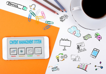 Content Management System concept. Mobile phone and coffee cup on a white office desk.