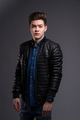 Fototapeta premium Casual young man in black jacket, jeans and boots on black background. Studio shoot.
