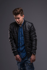 Fototapeta premium Casual young man in black jacket, jeans and boots on black background. Studio shoot.