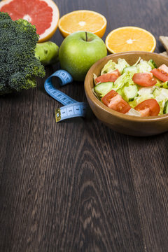 Food for diet and measuring tape on a dark wooden table.