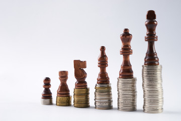 Growing coins stacks on white background. Black chess figures standing on coins meaning power and career growth. Financial growth, saving money, business finance wealth and success concept.