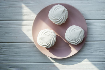 White sweet marshmallow air and gentle pink round dish on a white wooden table