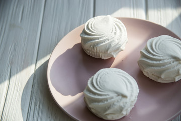 White sweet marshmallow air and gentle pink round dish on a white wooden table