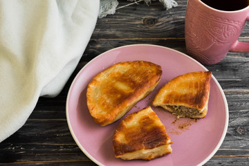 Pasties with meat, and a mug of tea on a wooden table in a rustic style.