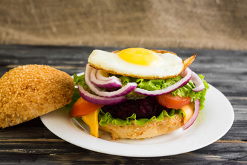 Hamburger with fried eggs and beetroot on a wooden table and ingredients