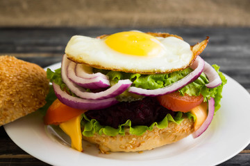 Hamburger with fried eggs and beetroot on a wooden table and ingredients
