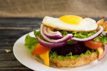 Hamburger with fried eggs and beetroot on a wooden table and ingredients