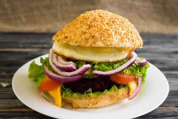 Hamburger with fried eggs and beetroot on a wooden table and ingredients