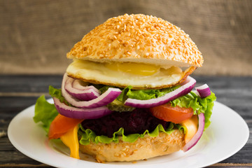 Hamburger with fried eggs and beetroot on a wooden table and ingredients
