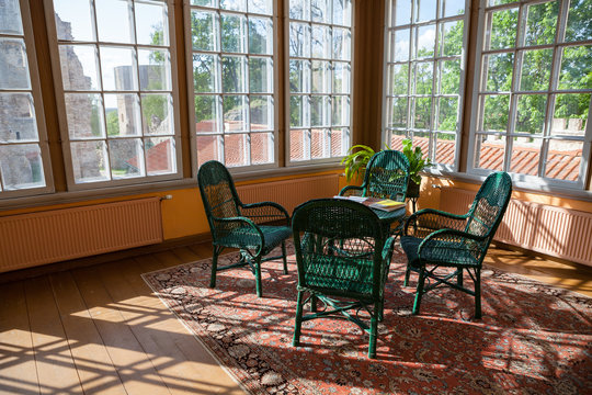 Bright room in cottage with wicker rattan chairs and table. Big windows and sunlight.