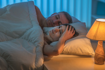 The depressed woman lie with man on the bed. Evening night time