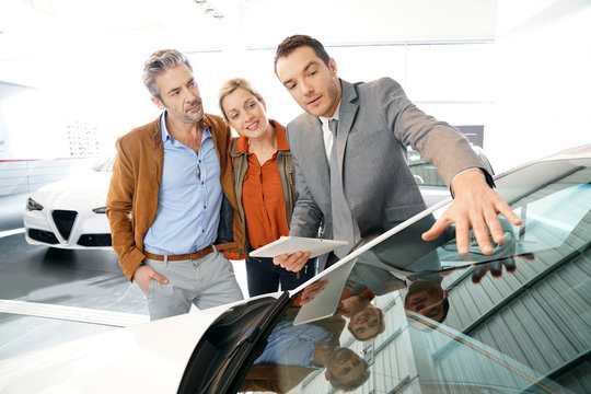 Car seller with couple in car dealership
