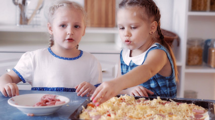 Obraz na płótnie Canvas Little girls sprinkle pizza with cheese
