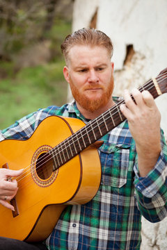 Hipster man with red beard playing a guitar