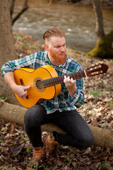 Hipster man with red beard with a guitar in the field