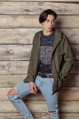 Handsome man wearing green jaket and torn jeans in wooden rural house interior