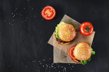 Craft beef burgers with vegetables. Flat lay on black textured background with sesame seeds.
