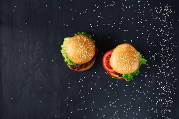 Craft beef burgers with vegetables. Flat lay on black textured background with sesame seeds.